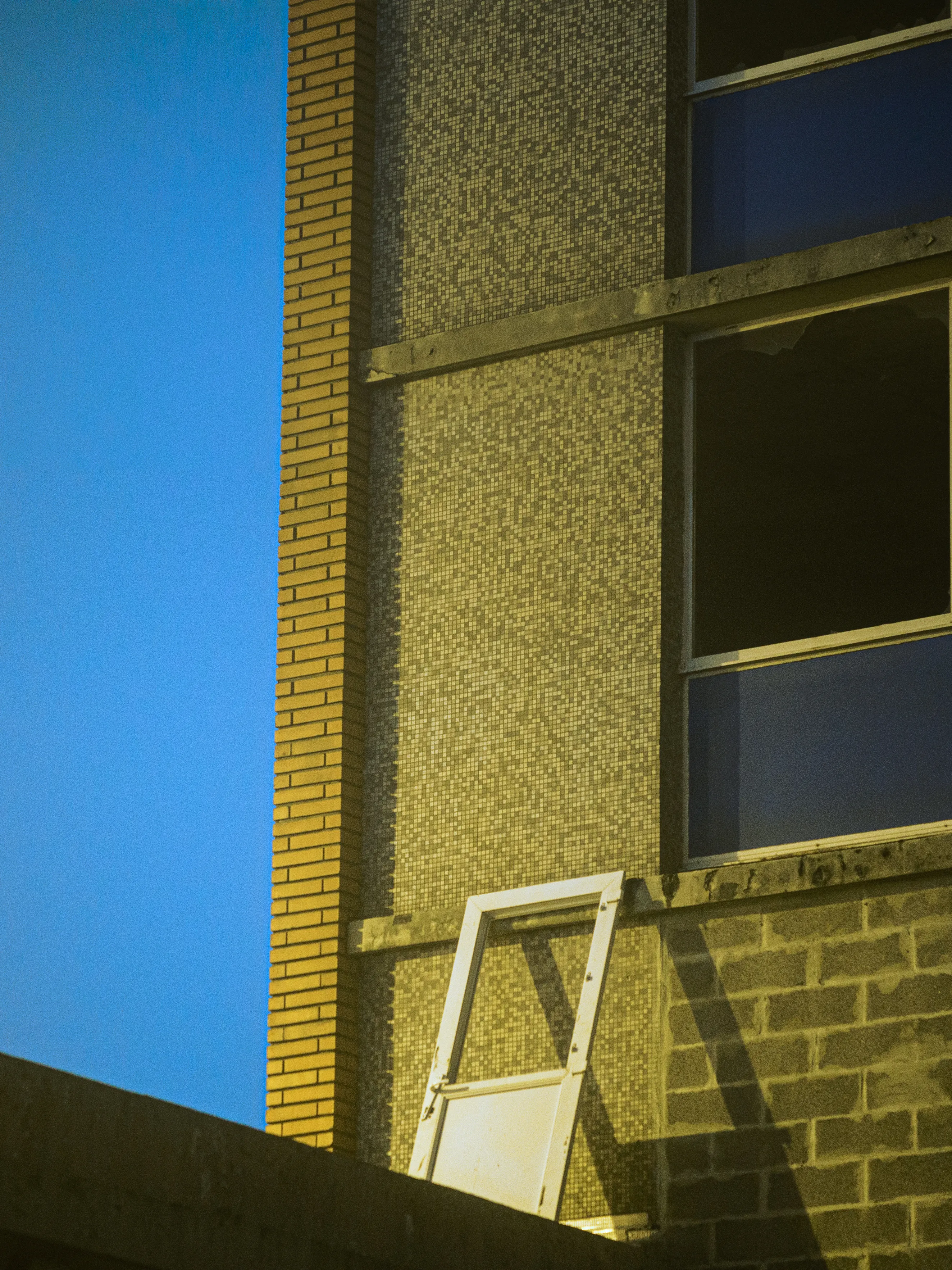 A brick and concrete building corner in hard sunlight against a painted blue wall