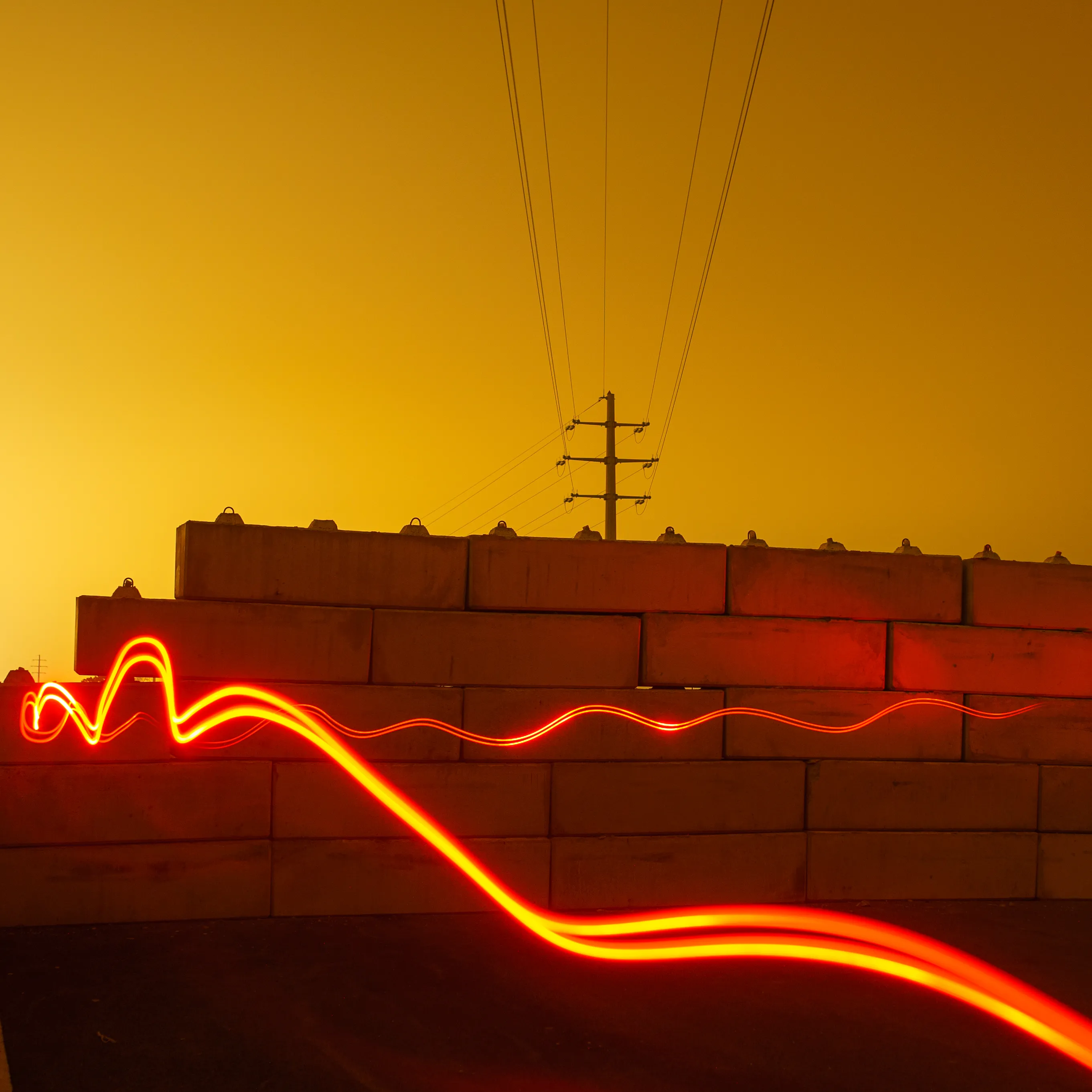 A brick wall under an orange sodium sky with power lines above, a loop of red light painted across the foreground