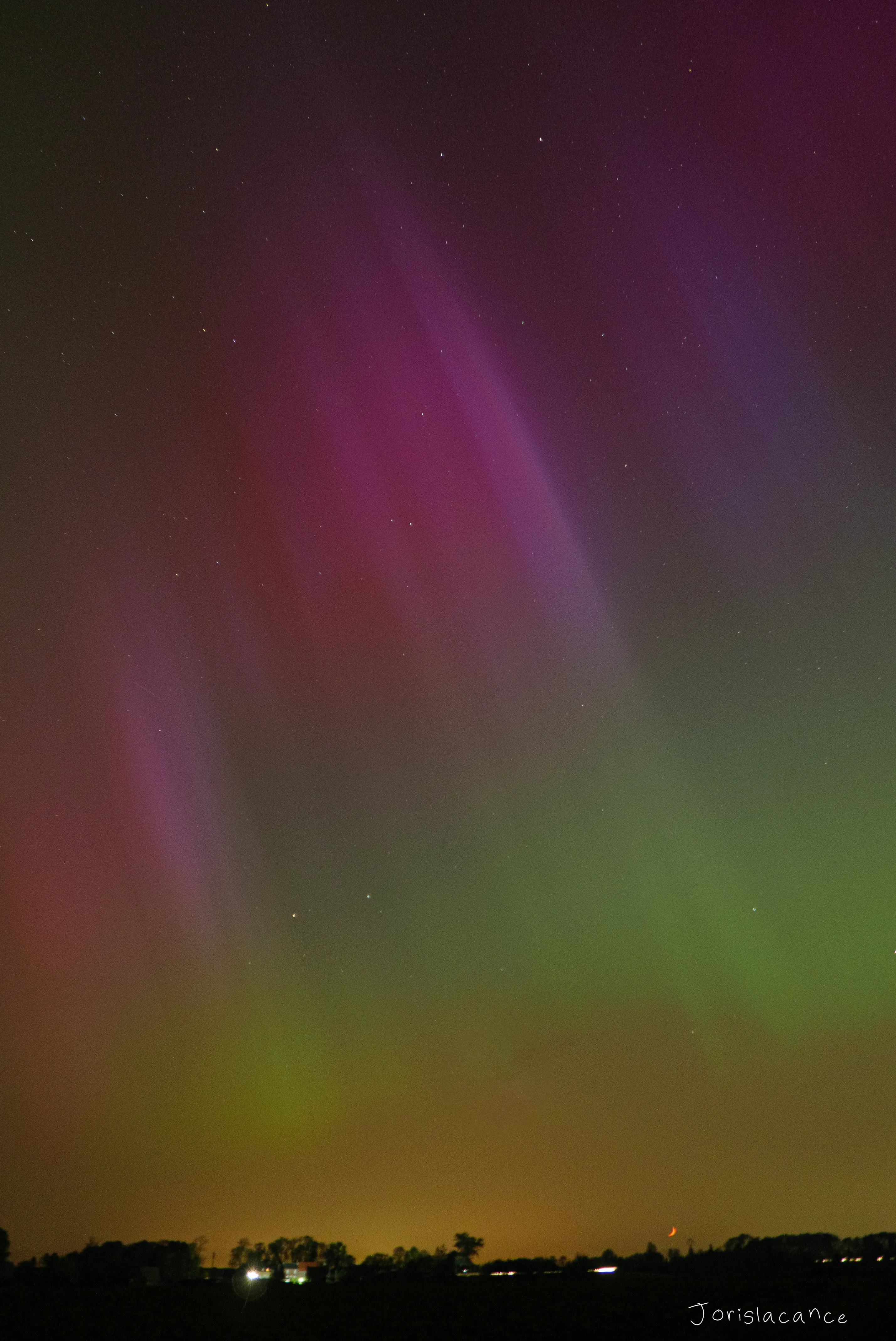 Pink and green aurora curtains standing over a distant horizon of town lights
