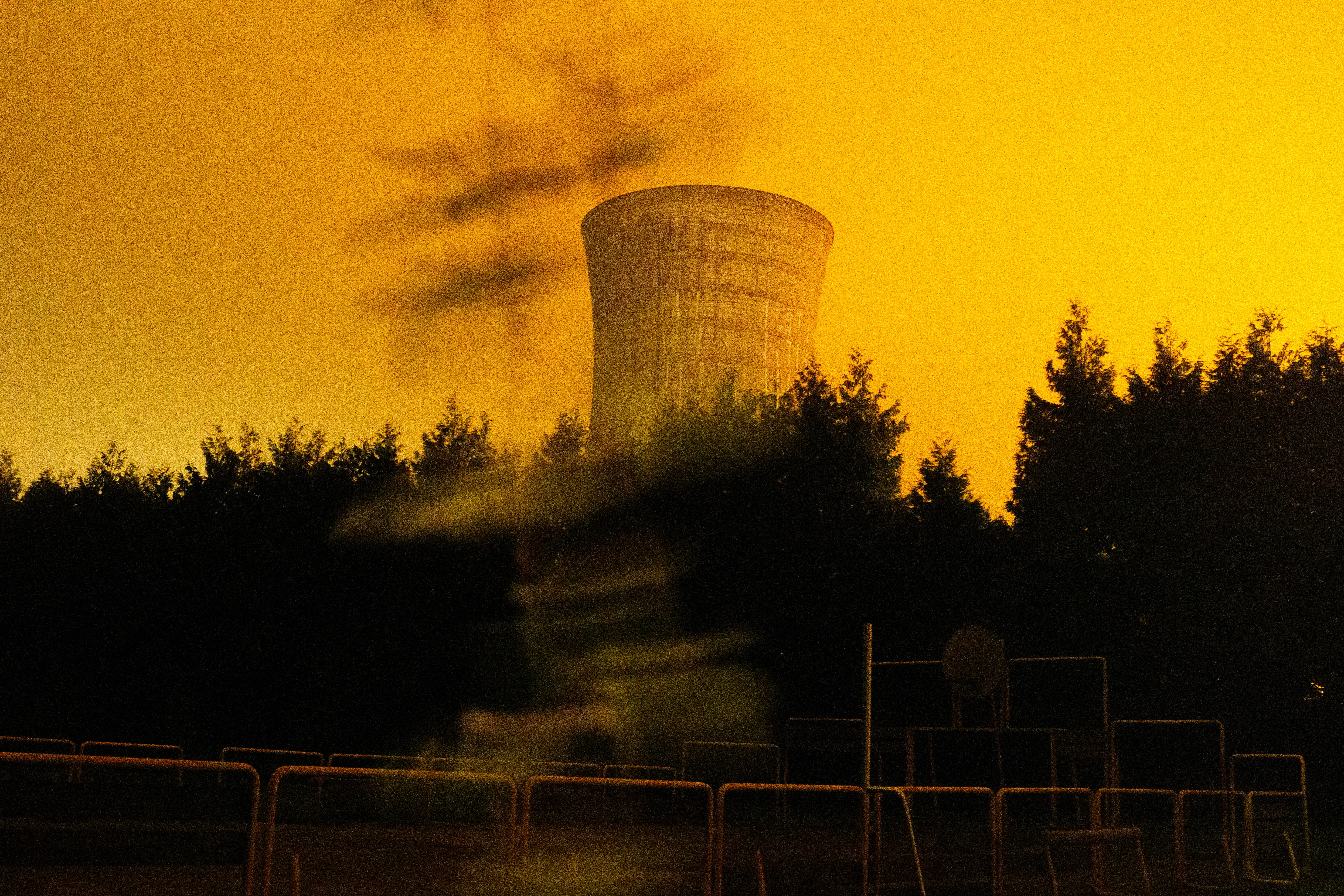 A cooling tower silhouetted against an orange sodium sky, a figure blurred by the long exposure in front of it
